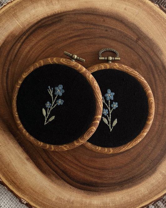 Two embroidery pieces with floral designs on a wooden surface.
