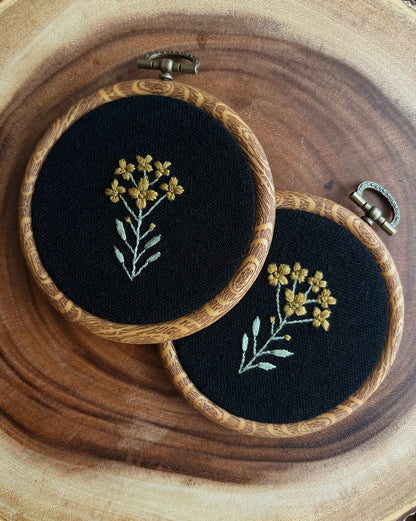 Two embroidered hoops with floral designs on a wooden surface