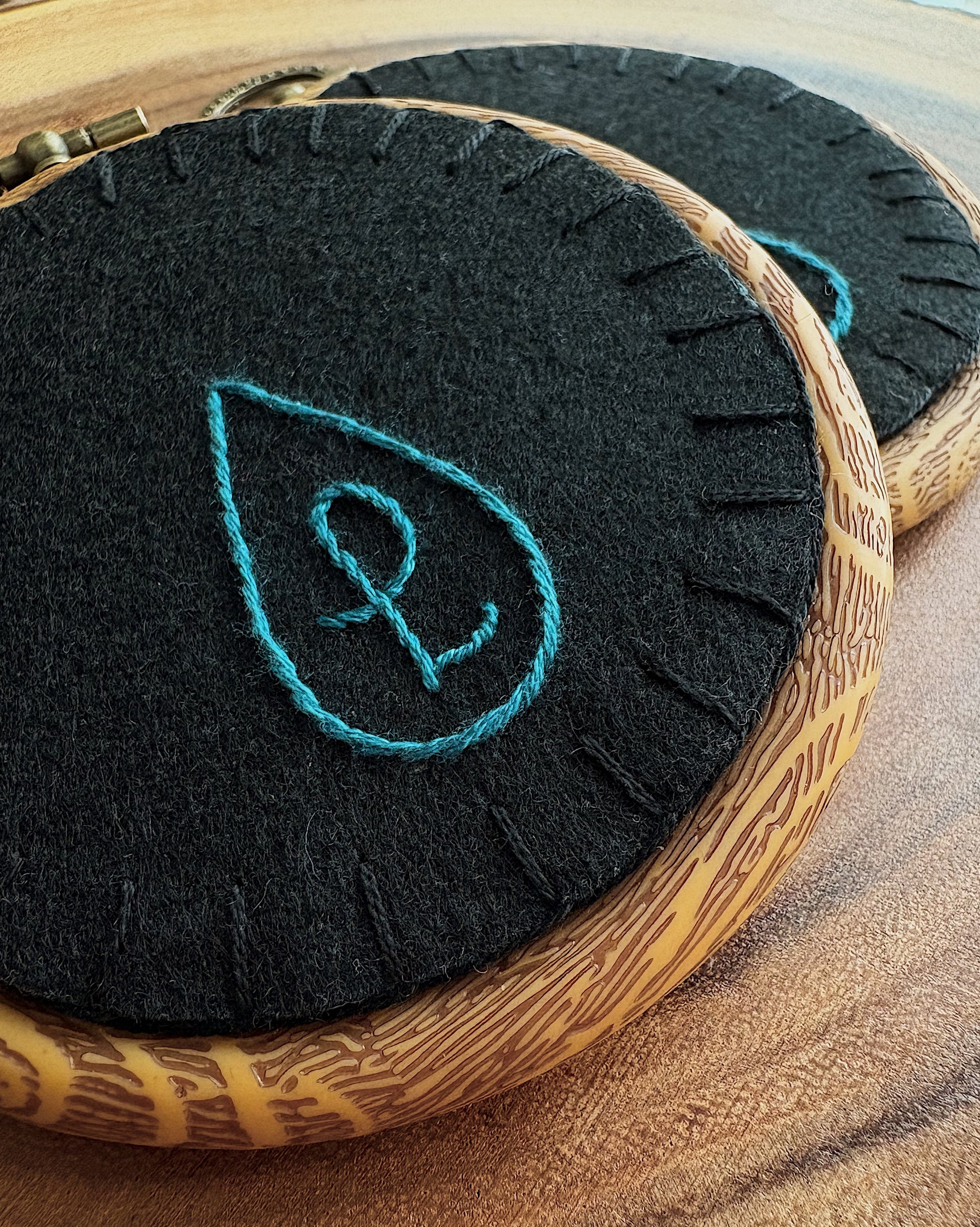 Felt stitched back with a teal monogram on a wooden surface