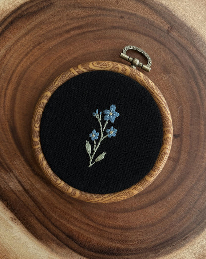 Embroidery of blue flowers in a wooden hoop on a wooden surface